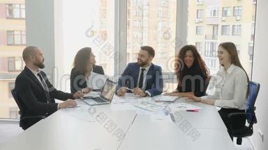办公室工作人员坐在一张方桌旁讨论合同的所有问题，两个人握手`